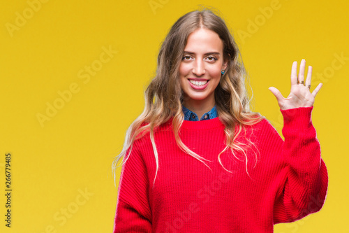 Beautiful young blonde woman wearing winter sweater over isolated background showing and pointing up with fingers number five while smiling confident and happy.