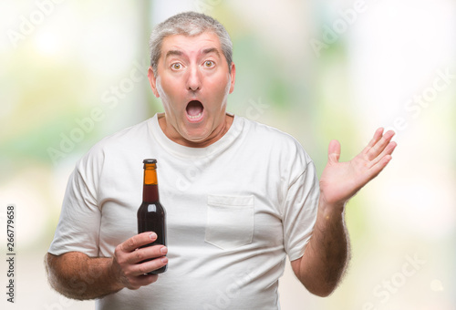 Handsome senior man drinking beer bottle over isolated background very happy and excited, winner expression celebrating victory screaming with big smile and raised hands