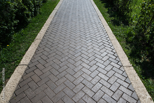 Paving slabs in the green garden. Texture of road tiles with herringbone pattern. Perspective view