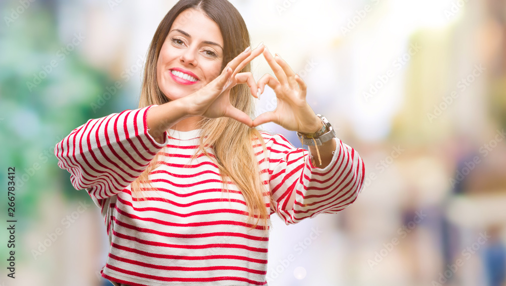 Young beautiful woman casual stripes winter sweater over isolated background smiling in love showing heart symbol and shape with hands. Romantic concept.