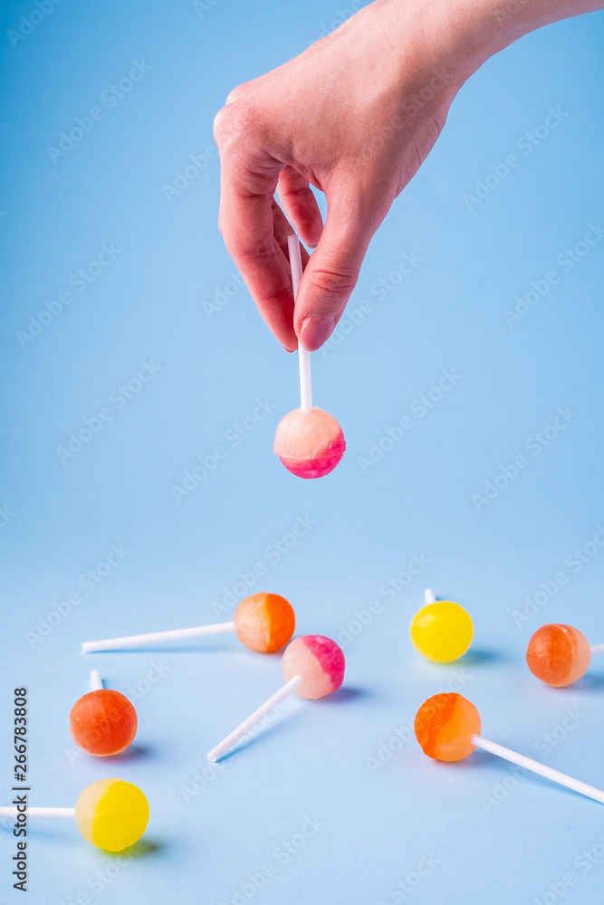 Woman holding in hand upside down lollipop candy on blue background