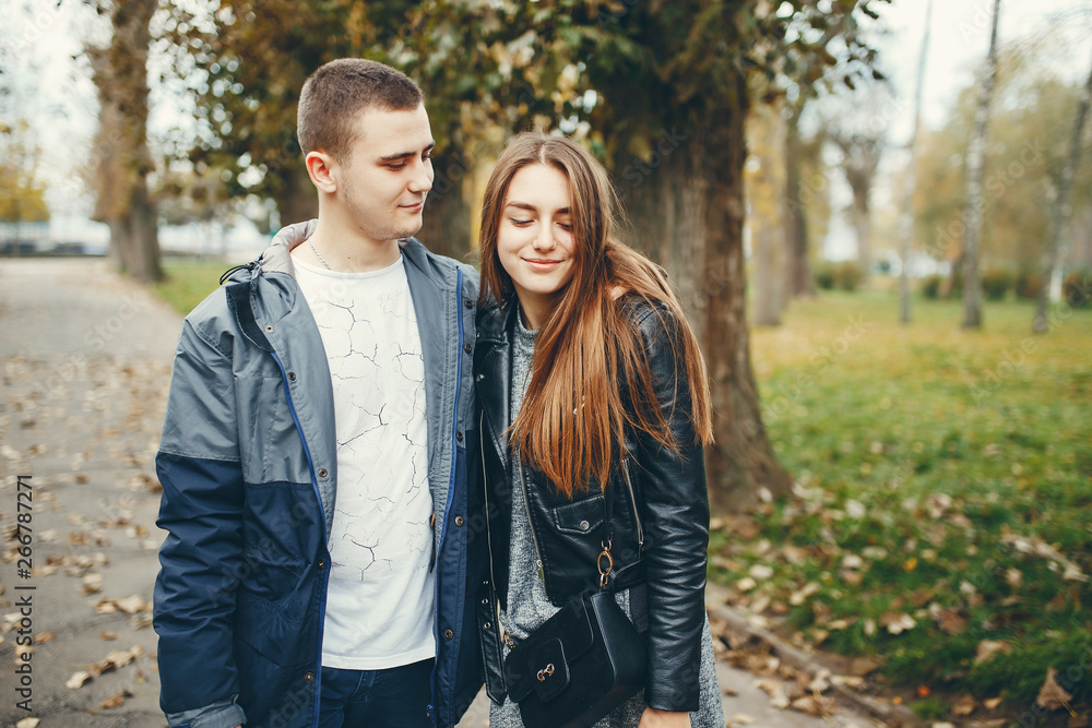 Cute couple walking in a autumn park. Boy in a black jacket. Girl in a gray dress Cute couple walking in a autumn park. Boy in a black jacket. Girl in a gray dress
