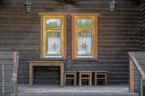 wooden brown facade of a vintage house with two Windows. wooden table and stools against the wal