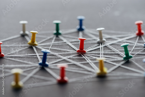 selective focus of colorful push pins connected with strings on grey, network concept