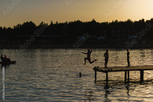 People jump from the pier into lake Issyk Kul. Guys swim in the lake at sunset. The texture of the surface of the water. Rest in Kyrgyzstan. photo