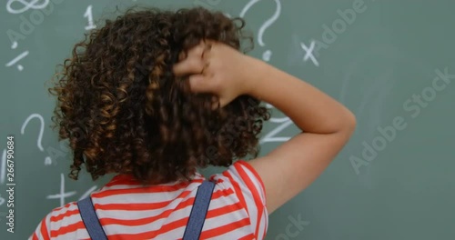 Rear view of mixed-race schoolgirl scratching her head in classroom at school 4k photo