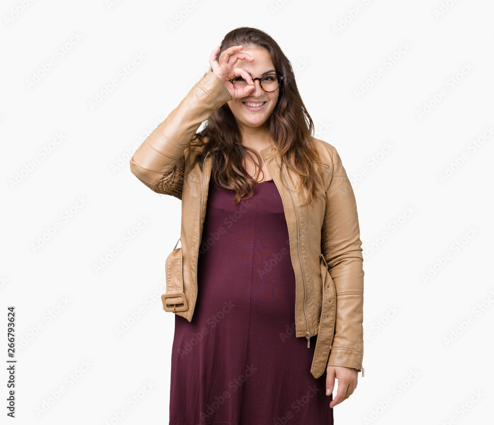 Beautiful plus size young woman wearing a dress and leather jacket over isolated background doing ok gesture with hand smiling, eye looking through fingers with happy face. Beautiful plus size young woman wearing a dress and leather jacket over isolated background doing ok gesture with hand smiling, eye looking through fingers with happy face.