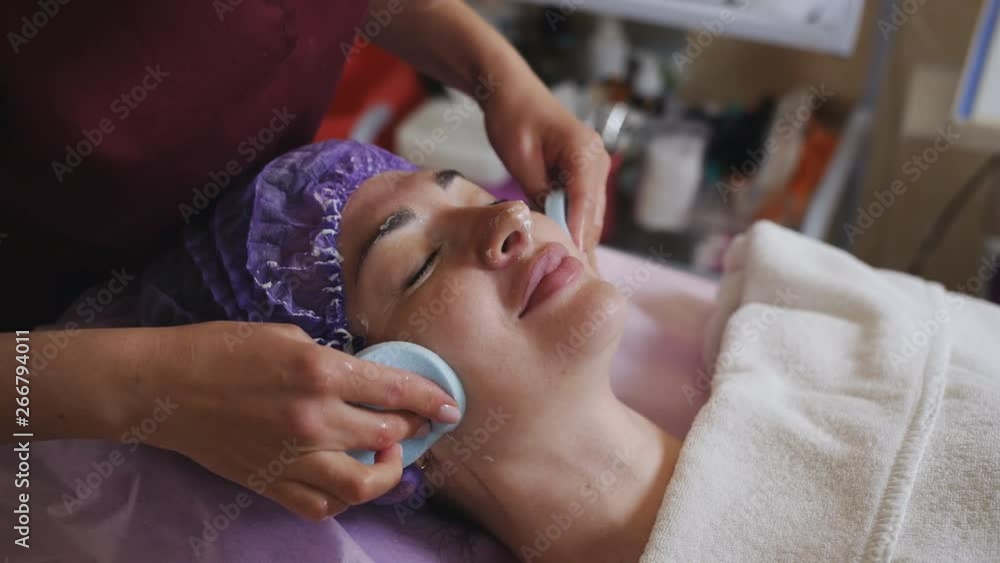 The beautician wipes the face of the patient after withdrawal of anti-aging cosmetic mask. The beautician wipes the face of the patient after withdrawal of anti-aging cosmetic mask.