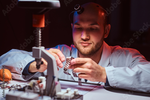 Expirienced watchmaker is doing engraving for custmer's watch at his workshop. photo