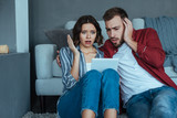 shocked man and woman gesturing while watching video on digital tablet