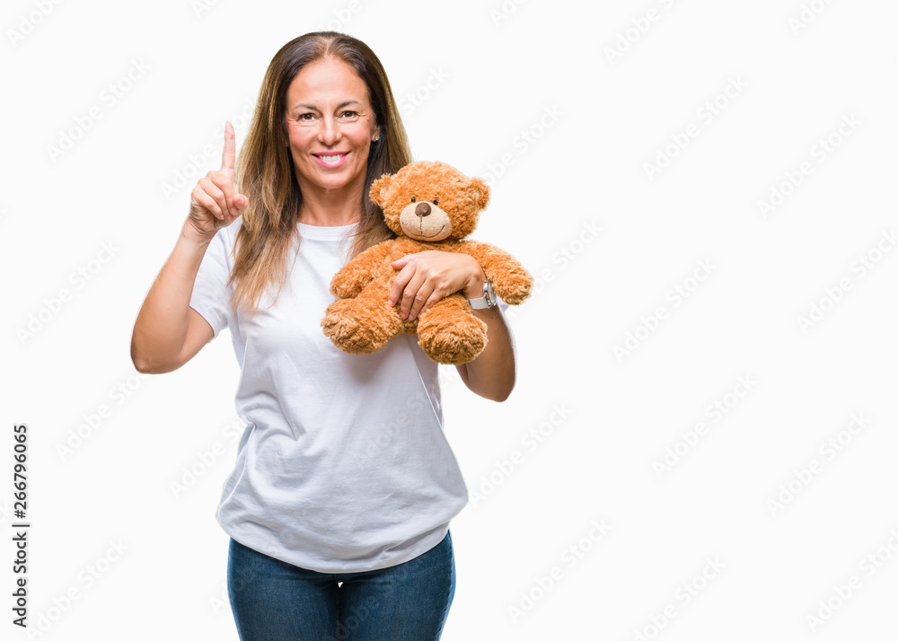 Middle age hispanic woman holding cute teddy bear plush over isolated background surprised with an idea or question pointing finger with happy face, number one Middle age hispanic woman holding cute teddy bear plush over isolated background surprised with an idea or question pointing finger with happy face, number one