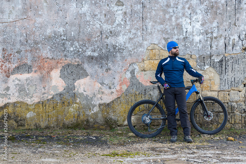 A guy in sportswear riding clothes on a modern mountain carbon bike with an air suspension fork at a vintage brick concrete wall.  © Mountains Hunter