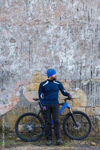 A guy in sportswear riding clothes on a modern mountain carbon bike with an air suspension fork at a vintage brick concrete wall. 