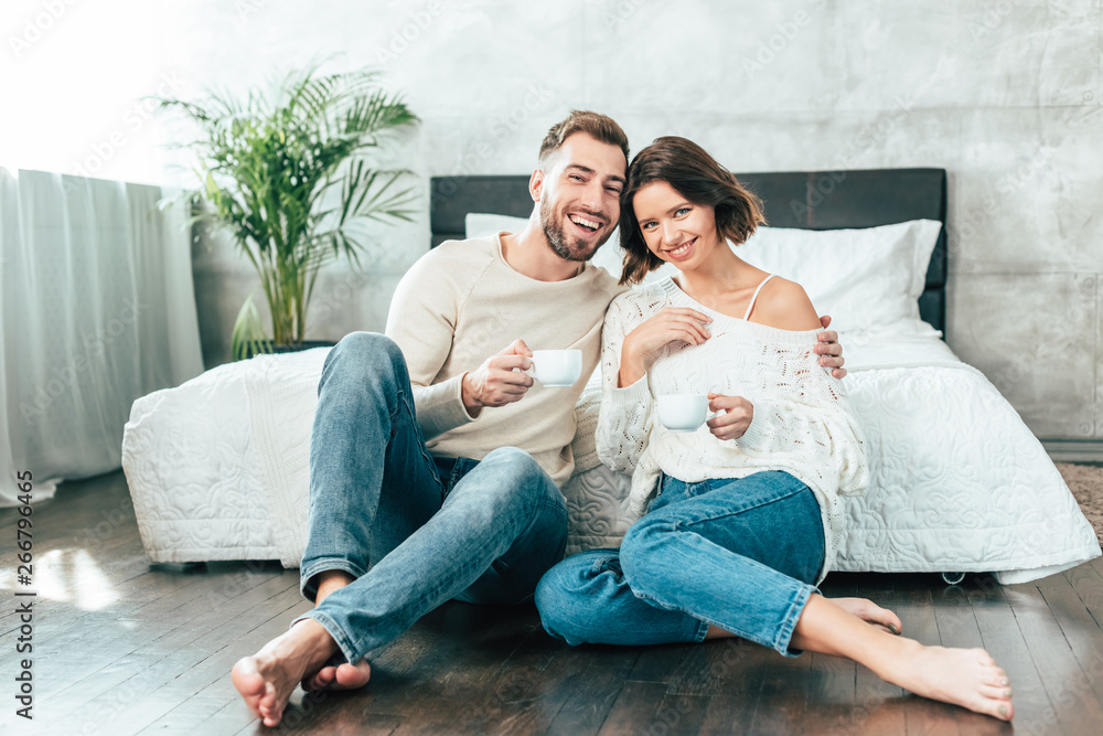 handsome man hugging beautiful woman and sitting on floor with cup handsome man hugging beautiful woman and sitting on floor with cup