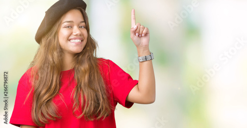 Young beautiful brunette fashion woman wearing red t-shirt and black beret over isolated background pointing finger up with successful idea. Exited and happy. Number one.