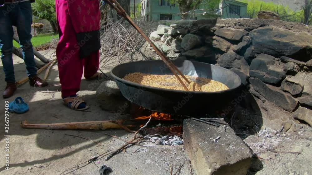 Handheld, exterior, medium wideshot of seeds or kernels being heated up in large pan over open flame. Handheld, exterior, medium wideshot of seeds or kernels being heated up in large pan over open flame.