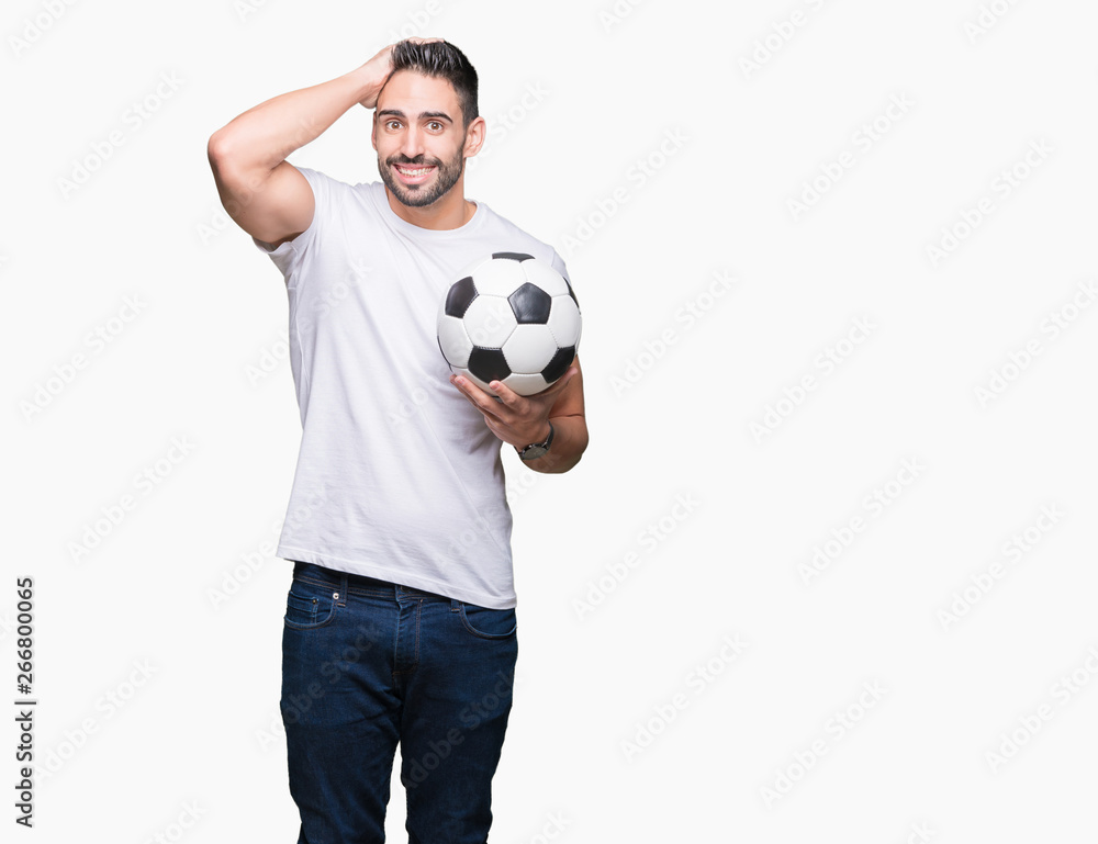 Young man holding soccer football ball over isolated background stressed with hand on head, shocked with shame and surprise face, angry and frustrated. Fear and upset for mistake.