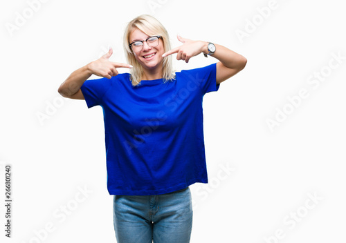 Young beautiful blonde woman wearing glasses over isolated background smiling confident showing and pointing with fingers teeth and mouth. Health concept.