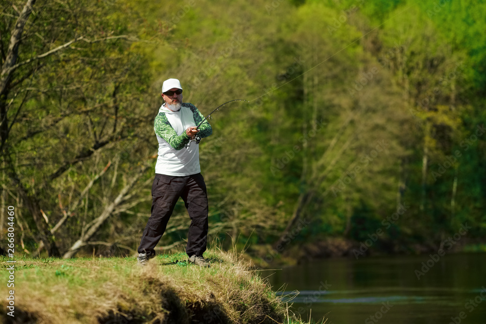 Naklejka premium Fisherman trying to do a perfect cast, throwing lure. Spining fishing, angling, catching fish. Hobby and vacation. Photo with shallow depth of field taken at wide open aperture.
