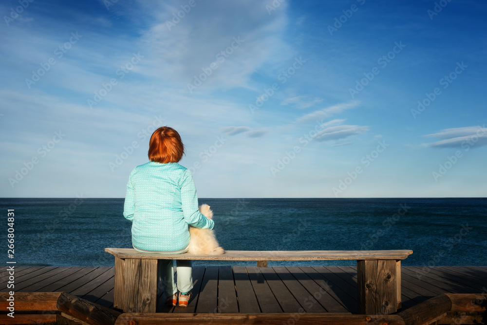 woman sitting with her pommeranian spitz puppy on a bench at the sea