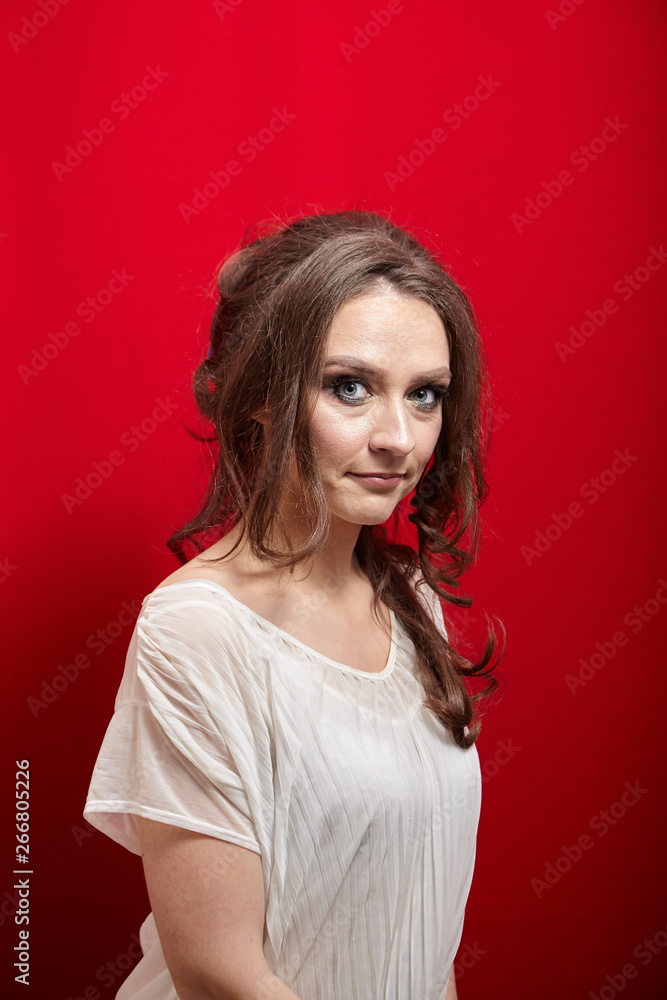 Portrait of young woman on red background. Attractive lady with long wavy brown hair in white blouse Portrait of young woman on red background. Attractive lady with long wavy brown hair in white blouse