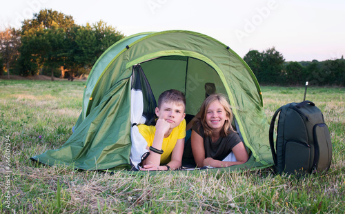 Smiling children lying in the tent in the park. Camping, tourism and teenagers activity or leisure concept.