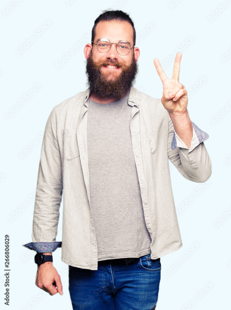 Naklejka premium Young blond man wearing glasses showing and pointing up with fingers number two while smiling confident and happy.