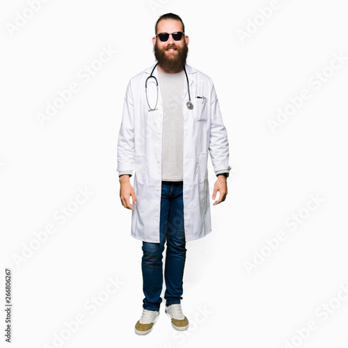 Young blond doctor man with beard wearing sunglasses with a happy and cool smile on face. Lucky person.