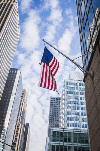 American flag floating among the skyscrapers in the streets of Manhattan in New York on a beautiful blue sky - New York City, NY, USA