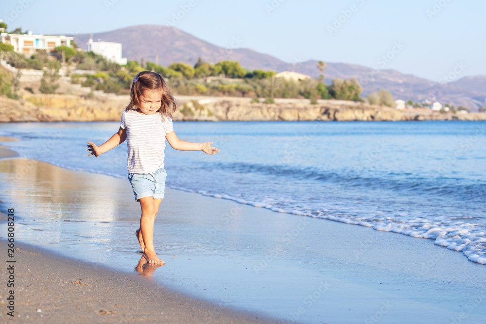 Adorable little girl walking along white sand beach