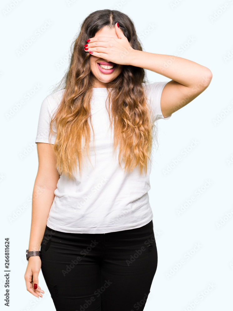 Young beautiful woman wearing casual white t-shirt smiling and laughing with hand on face covering eyes for surprise. Blind concept. Young beautiful woman wearing casual white t-shirt smiling and laughing with hand on face covering eyes for surprise. Blind concept.