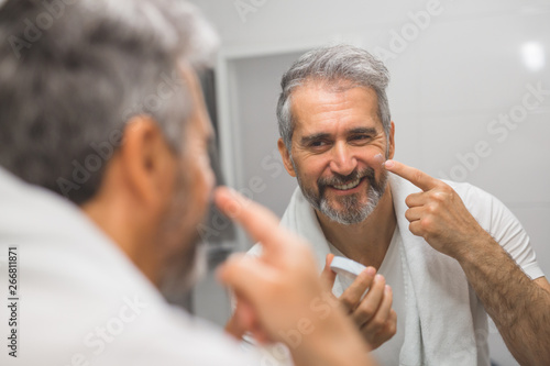 middle aged man using skin cream in bathroom
