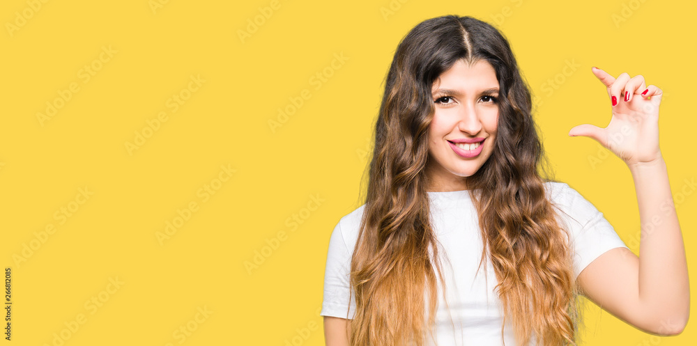 Young beautiful woman wearing casual white t-shirt smiling and confident gesturing with hand doing size sign with fingers while looking and the camera. Measure concept. Young beautiful woman wearing casual white t-shirt smiling and confident gesturing with hand doing size sign with fingers while looking and the camera. Measure concept.