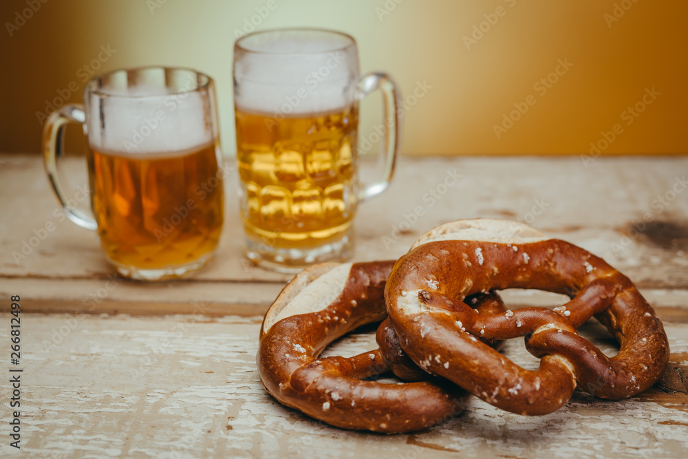 draft beer in the mugs and pretzels on wooden board against yellow background draft beer in the mugs and pretzels on wooden board against yellow background