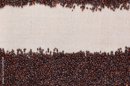 Roasted coffee beans in large amount with open space at top on linen canvas.