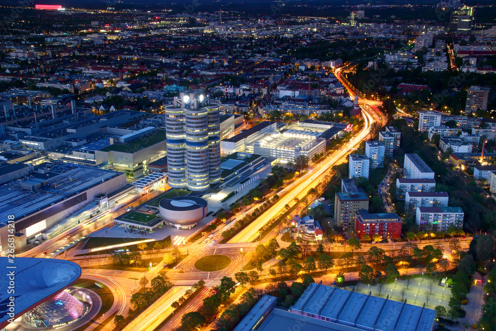 Fototapeta premium Modern European aerial cityscape in blue hour with broad circle road intersection, commercial, office and industrial buildings in outskirts lit by street and car lights, Munchen Bayern Germany Europe