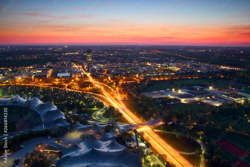 Naklejka premium Nowoczesna europejska panorama miasta w niebieskiej godzinie z biurowcami, wysokimi wieżowcami, parkami, wiaduktem i skrzyżowaniem autostrad na obrzeżach oświetlonych światłami samochodów, Moosach Milbertshofen Munchen Niemcy