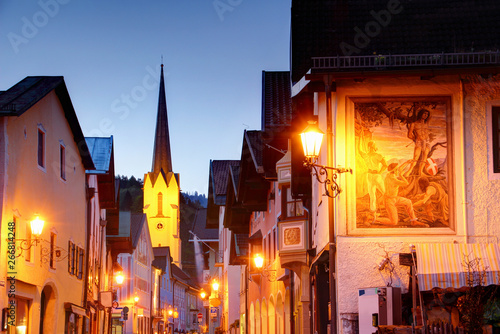 Narrow main street in blue hour in historic center of German resort town Garmisch Partenkirchen with row of old Bavarian painted houses and Maria Himmelfahrt Catholic church, Bayern Germany Europe