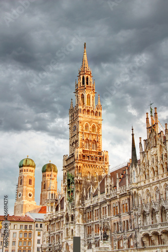 Tall spire of neo-Gothic town hall building Neues Rathaus and towers of Frauenkirche cathedral in historic main square Marienplatz in morning orange sunlight, Altstadt Munchen Bayern Germany Europe