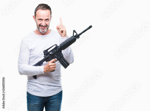 Middle age senior hoary criminal man holding gun weapon over isolated background surprised with an idea or question pointing finger with happy face, number one