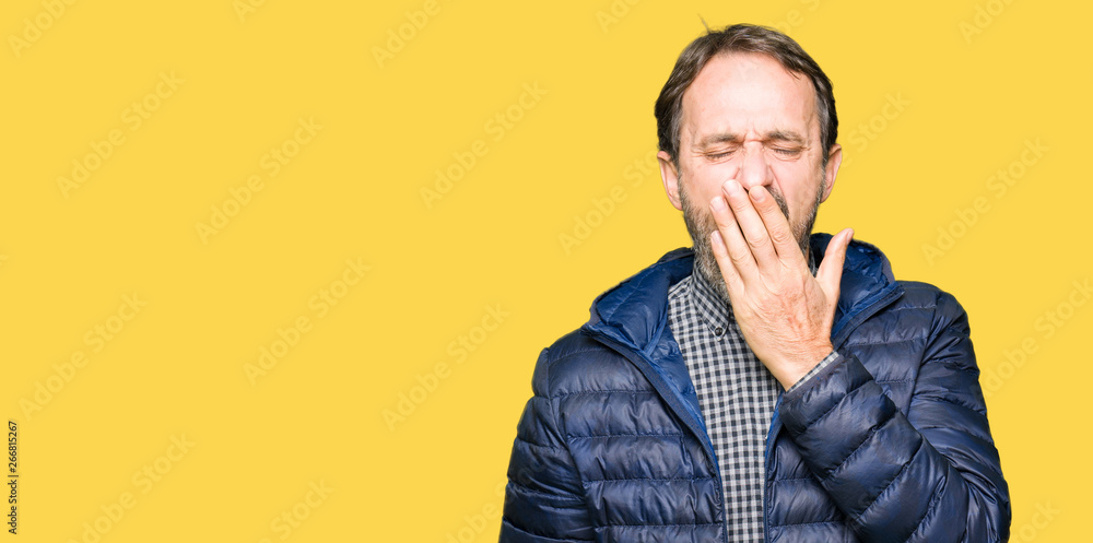 Middle age handsome man wearing winter coat bored yawning tired covering mouth with hand. Restless and sleepiness.