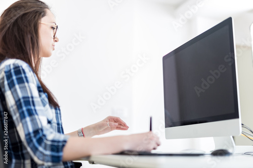 Young woman using digital pen with graphic tablet while working on computer.