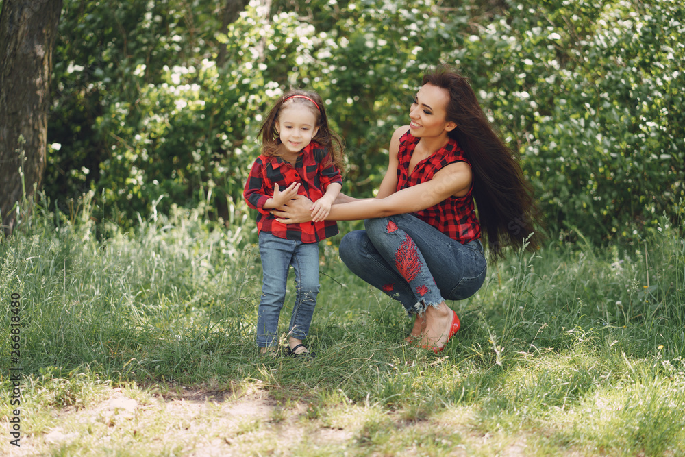 Fototapeta premium Young and very beautiful slim mum with long hair walking in a sunny summer park with her little beauties daughter