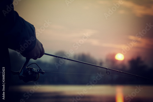 Fishing rod spinning close up. Fisherman on the background of a beautiful sunset.