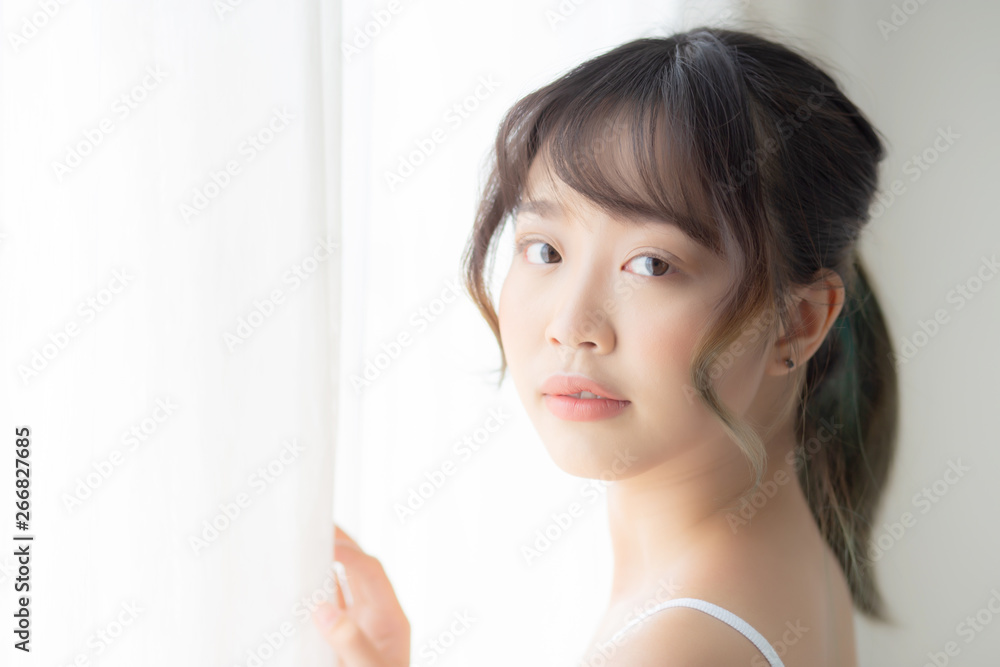 Portrait of beautiful young asian woman standing at the window and smile while wake up with sunlight at morning, girl happy with fresh and cheerful, lifestyle and relax for wellness concept. Portrait of beautiful young asian woman standing at the window and smile while wake up with sunlight at morning, girl happy with fresh and cheerful, lifestyle and relax for wellness concept.