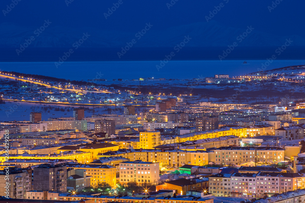 Naklejka premium Night cityscape. Top view of the port town. Bright street lighting at dusk. In the distance sea bay. Magadan, Siberia, Far East of Russia. Coast of the Sea of Okhotsk.