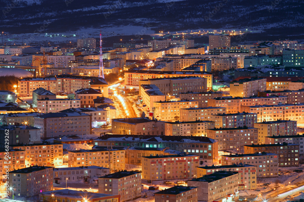 Aerial view of the night city. Beautiful cityscape with TV tower and many buildings. Bright street lighting at dusk. Top view of the city of Magadan, Siberia, Far East of Russia.