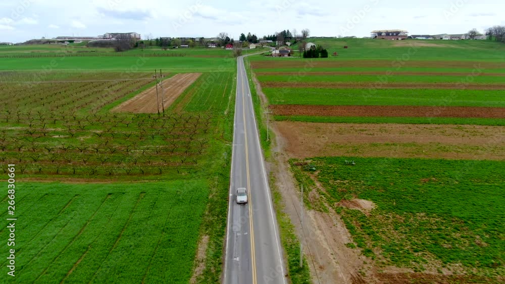 Aerial view of a car driving towards the viewer on a straight road in the American countryside, small residential area on top of hill in the background, travel and transportation concept Aerial view of a car driving towards the viewer on a straight road in the American countryside, small residential area on top of hill in the background, travel and transportation concept