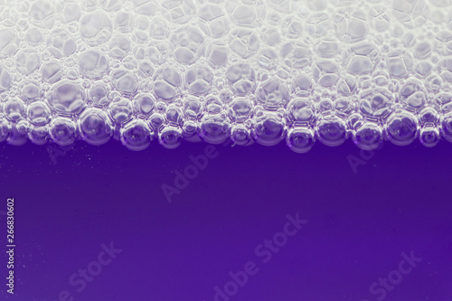 White bubbles resting on purple liquid. Side view with copy space. Background concept. Macro.