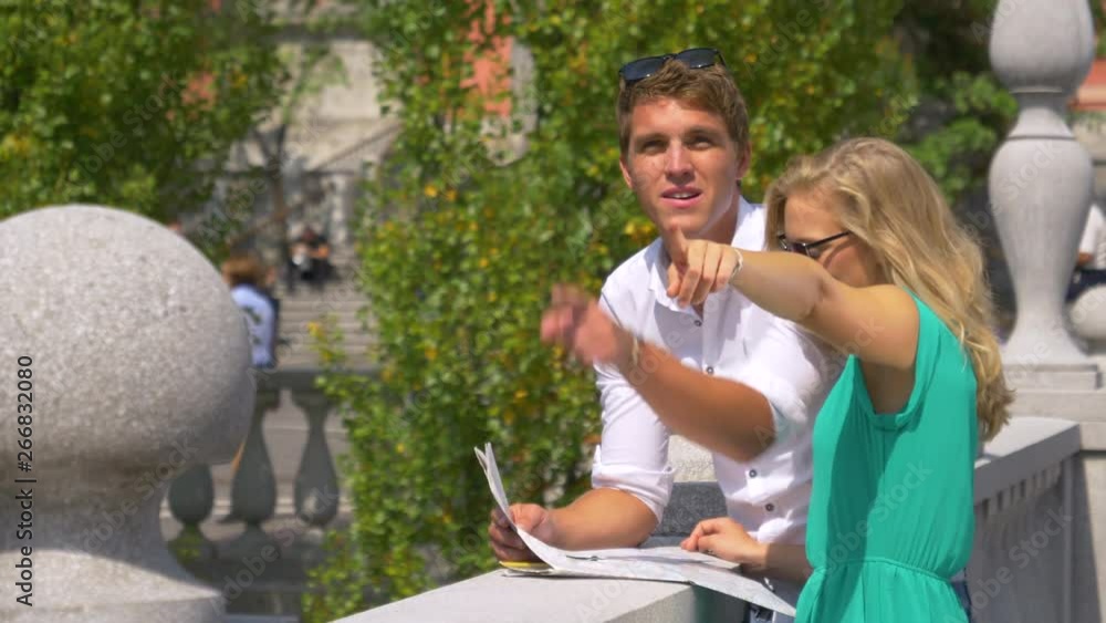 CLOSE UP, DOF, HANDHELD: Young Caucasian woman and her boyfriend observe the scenic city while looking at a map. Lost tourist couple looks at a map while exploring the beautiful streets of Ljubljana. CLOSE UP, DOF, HANDHELD: Young Caucasian woman and her boyfriend observe the scenic city while looking at a map. Lost tourist couple looks at a map while exploring the beautiful streets of Ljubljana.